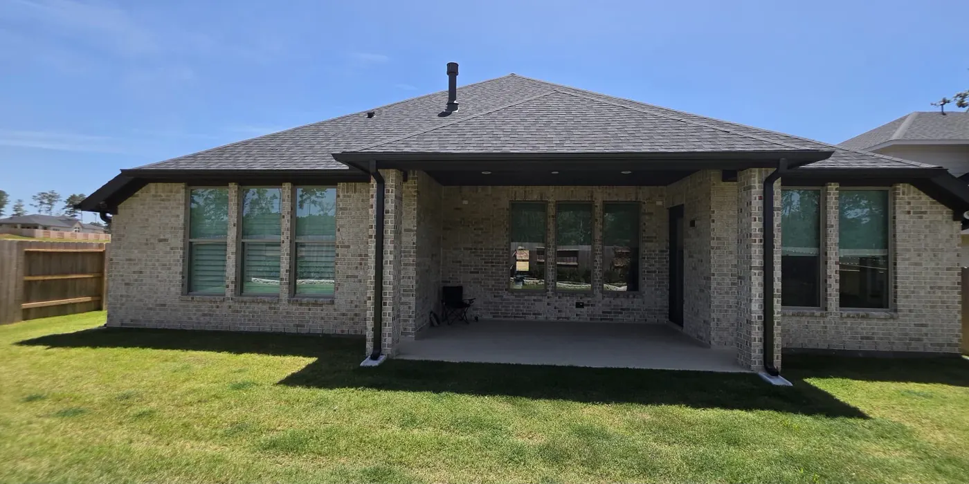 Back of a brick home with dark seamless gutters and downspouts around a covered patio