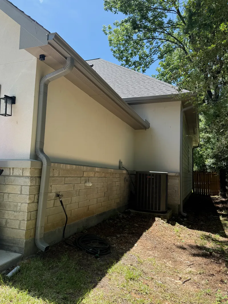 Close view of a gray seamless gutter and downspout along the side of a stucco and stone home
